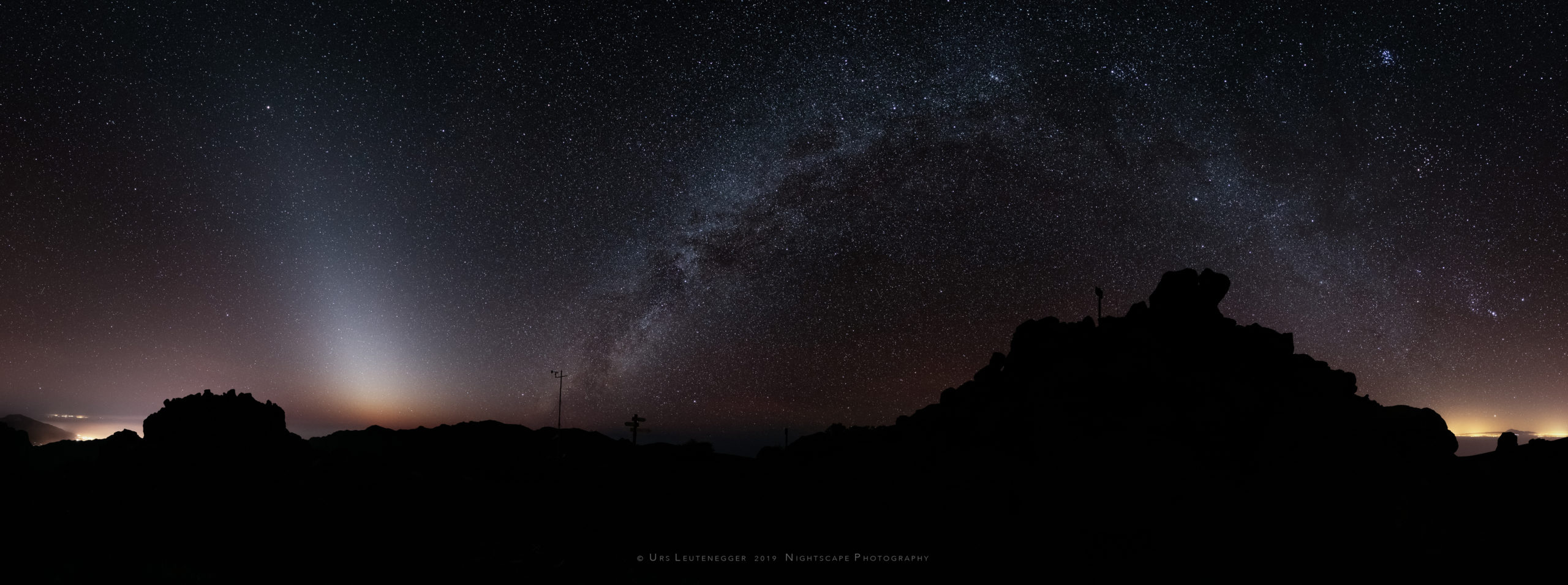 Zodiacal light with Milky Way over silhouette of Pico de la Cruz, La Palma. Light pollution from Los Llanos de Aridane and Tenerife at horizon.