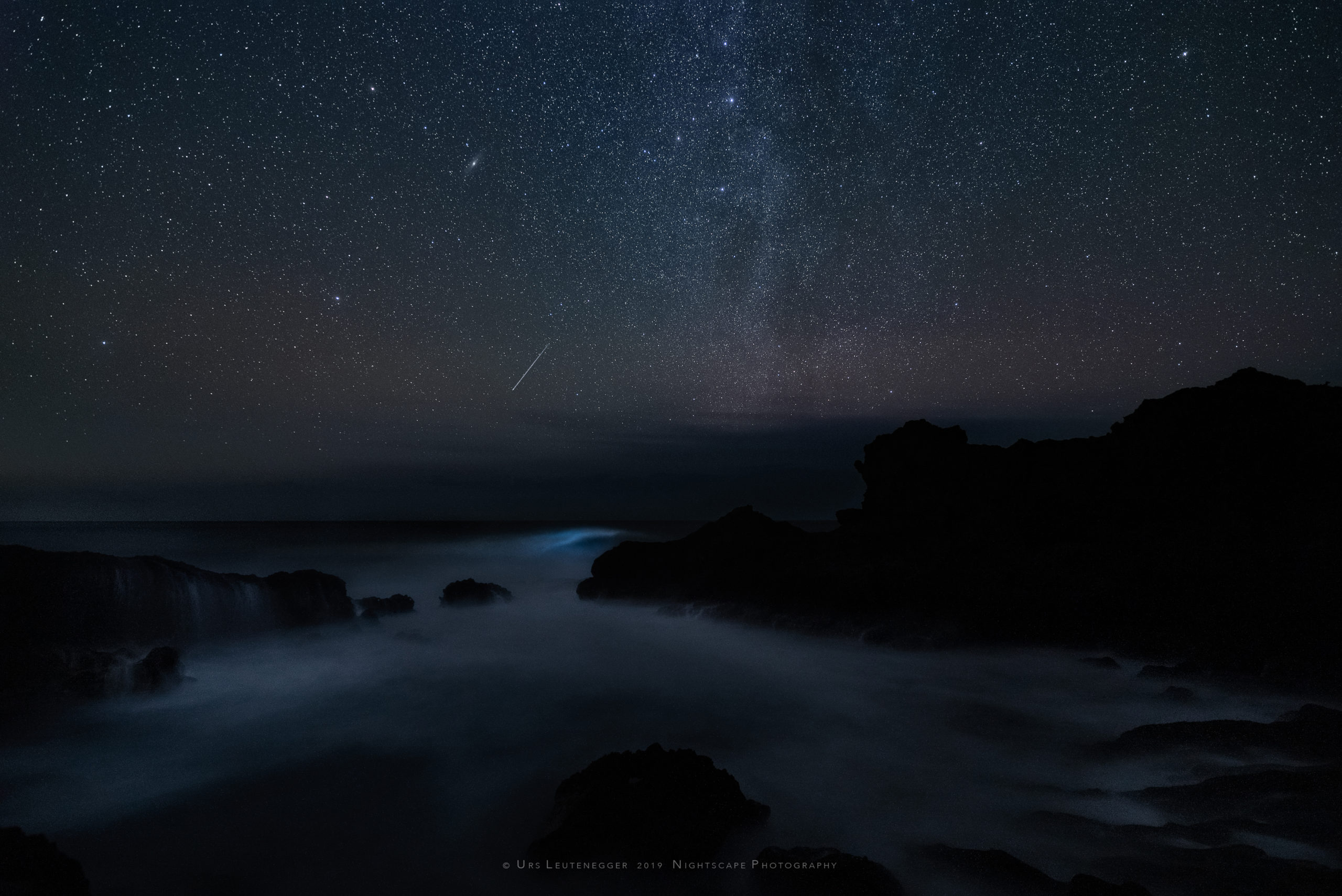 Vertical Milky way over Atlantic Ocean, Cassiopeia and Andromeda, bioluminescence in sea wave, single meteor hitting atmosphere close to horizon. Natural night sky glow. Northwest of La Palma.